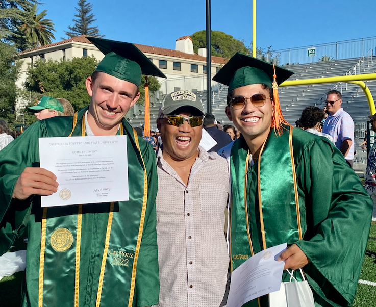 Enzo and a friend in green graduation gowns with their father/mentor at Cal Poly commencement ceremony